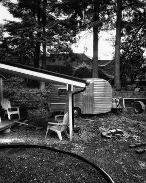 Black and white photograph of a fifth wheel trailer parked near a deck outside of a house in Portland Oregon